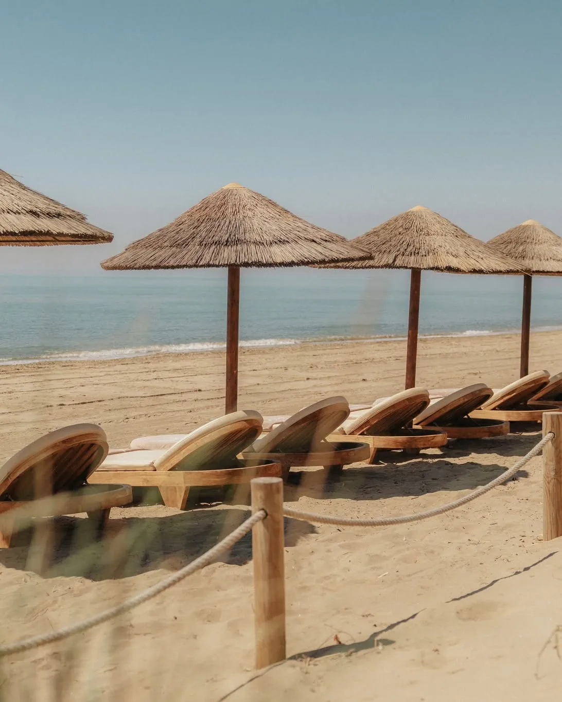 Rows of wooden beds under thatched parasols facing a calm sea