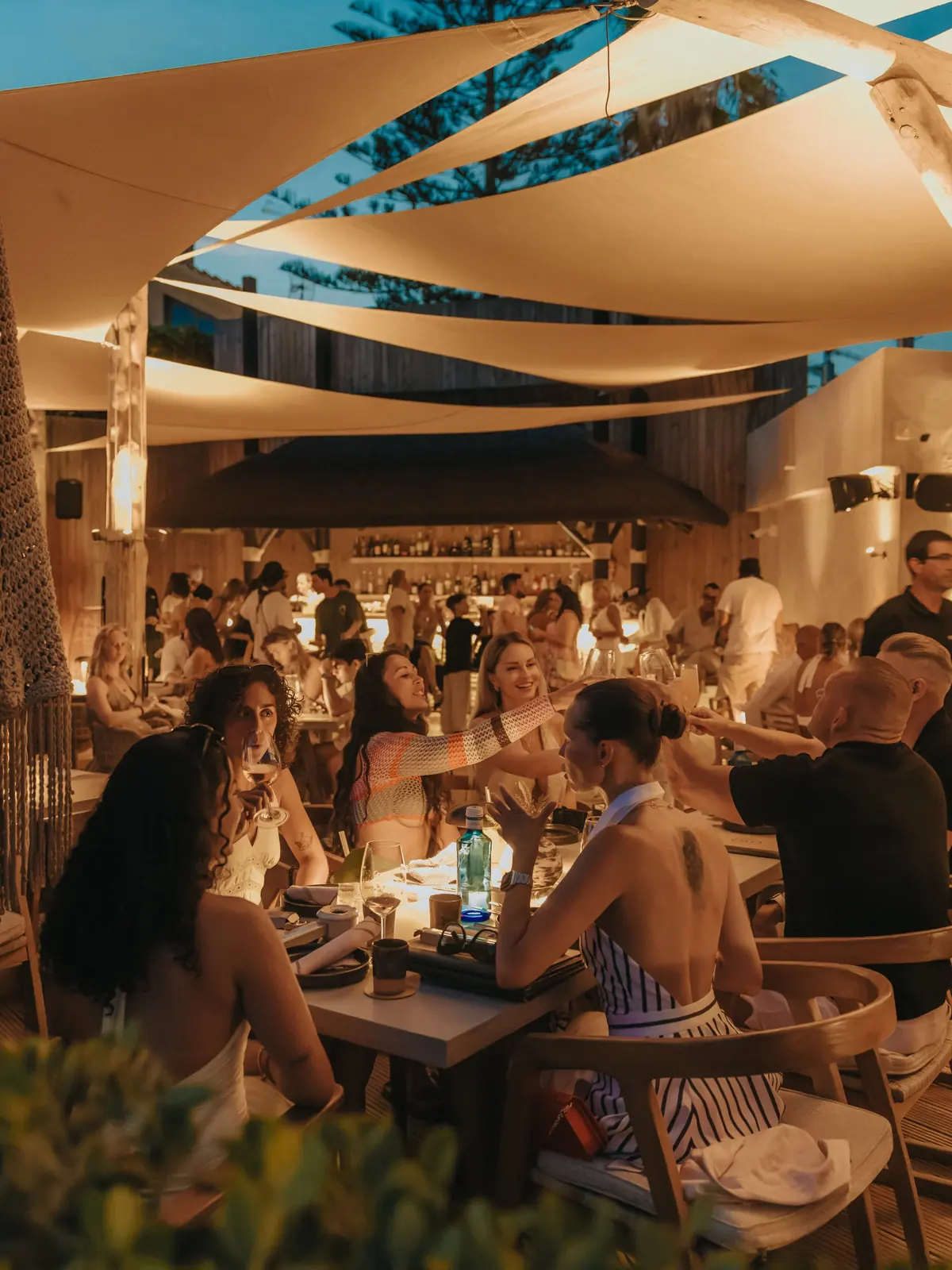 The terrace at nightfall under the sail shades, the bar lit behind