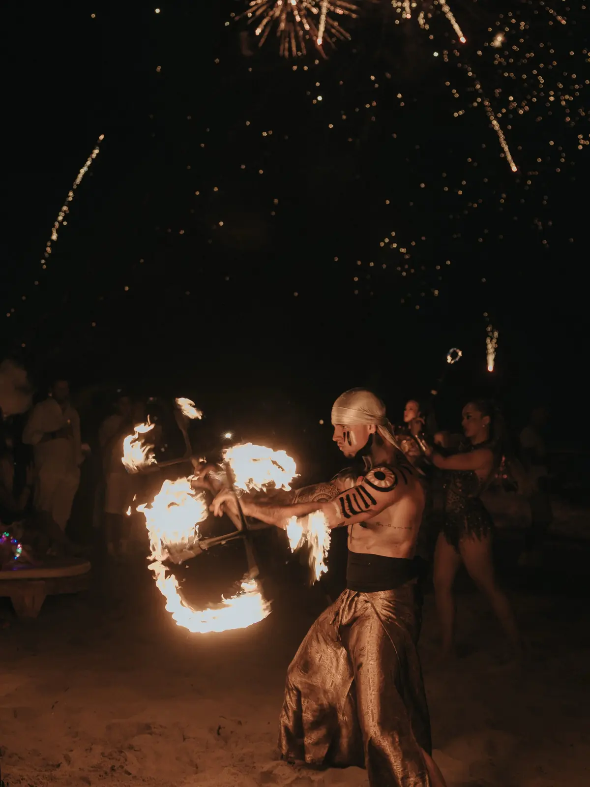 A fire hoop and fireworks above the sand