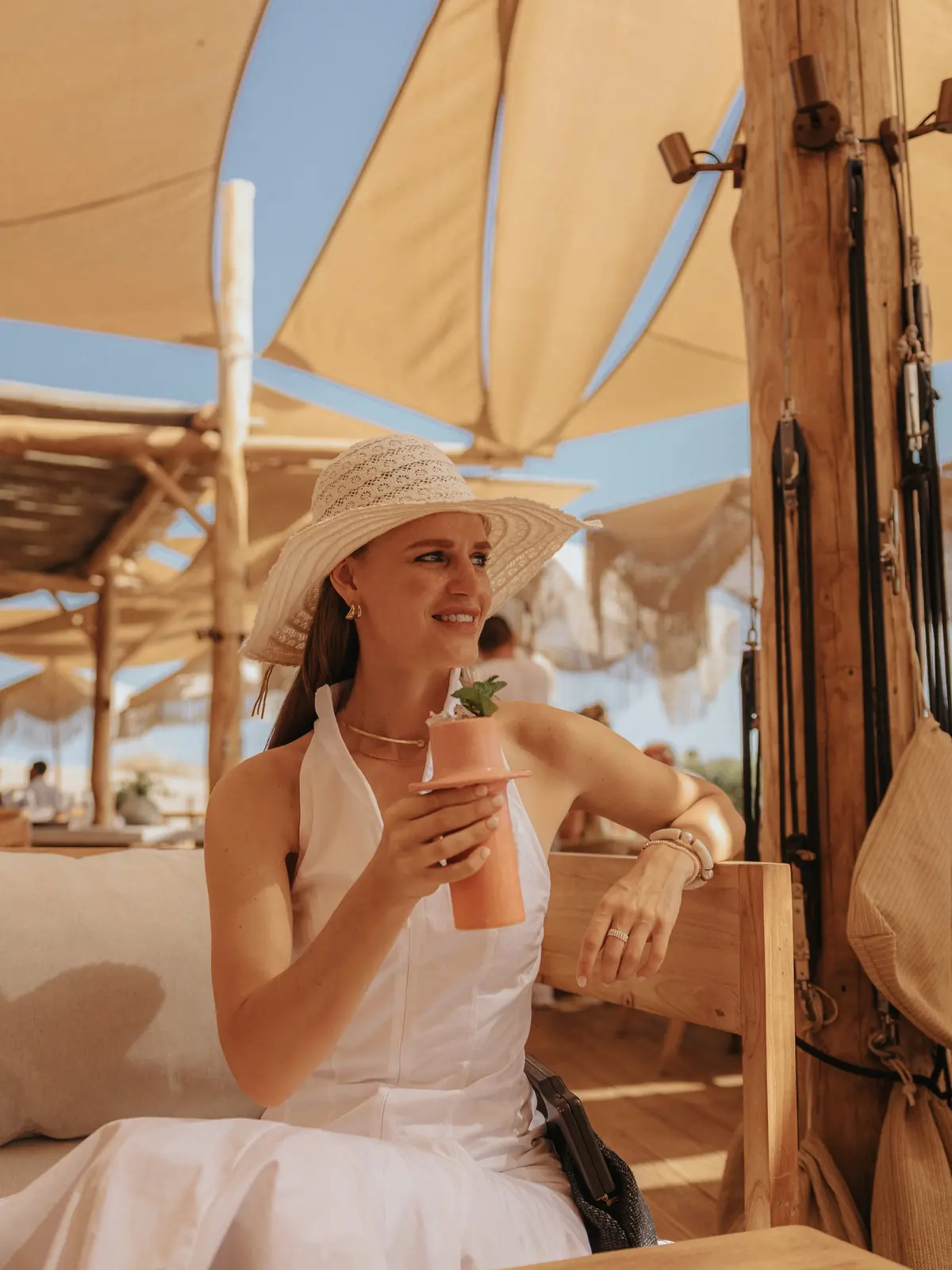 A guest in a straw hat with a cocktail under the terrace sail shades